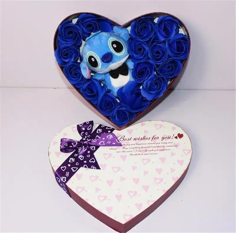 La peluche bleue de Stich est dans une boite en forme de coeur. Il y a des roses bleues tout autour de lui. Sur le couvercle de la boîte, il y a un ruban violet des inscriptions et des motifs coeurs. Stich porte un noeud papillon noir.