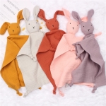 Cinq doudous à l'effigie d'un lapin en différentes couleurs mis ensemble sur un tissu de couleur clair