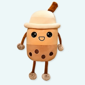 Peluche Bubble tea avec un chapeau , elle est beige et marron, et se trouve assise sur l'accoudoir en bois d'un fauteil à carreaux beige, blanc et marron