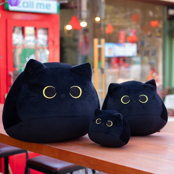 Trois peluches chats noires de trois tailles différentes. Posées sur une table en bois.