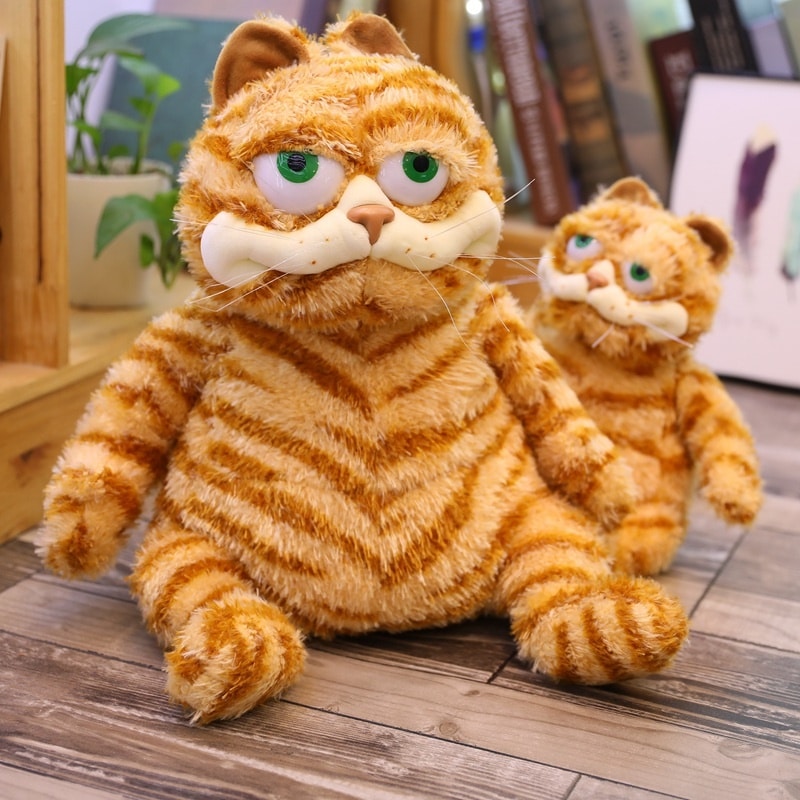 Deux peluches du même modèle d'un chat tigré roux assis sur un support en bois, le premier grand et celui en arrière-plan de petite taille