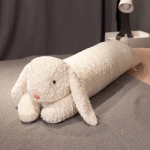 on voit une peluche coussin lapin géant blanc posé sur un lit avec des draps gris