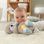 On voit un bébé sur un lit avec une peluche loutre pour bébé grise et le dessous des pattes bleues
