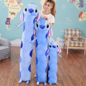 on voit trois peluches géantes de Stitch extra longue les unes à côtés des autres debout, elles sont bleues et une femme adulte se tient à côté pour montrer la hauteur des peluches