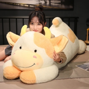 on voit une femme asiatique sur un lit couchée sur une peluche vache adorable géante noir et beige avec deux petites cornes